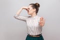 Portrait of ignoring beautiful young woman in striped shirt with makeup and collected ban hairstyle, standing with stop gesture Royalty Free Stock Photo