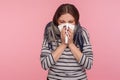 Portrait of ill woman wrapped in warm scarf sneezing in napkin, cleaning runny nose, suffering allergy