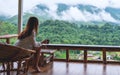 A beautiful asian woman holding and drinking hot coffee , sitting on balcony and looking at mountains and green