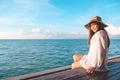 Portrait image of a happy beautiful asian woman on white dress sitting on wooden balcony by the sea with clear blue sky Royalty Free Stock Photo