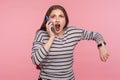Portrait of impatient woman in striped sweatshirt talking on mobile phone and looking with shocked angry expression