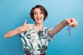 Portrait of impressed friendly woman with stylish hairdo wear print shirt give you keys show thumb up isolated on blue