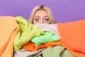 Portrait of impressed terrified girl hiding face behind big pile stack clothes isolated on purple color background