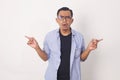 Portrait of indecisive, confused asian man asking show way, pointing sideways, left and right, asking what variant pick Royalty Free Stock Photo