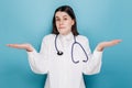 Portrait of indecisive woman doctor in white coat, shrugging and looking troubled answer, dont know, isolated on blue wall