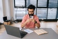 Portrait of Indian business man in elegant glasses using mobile phone texting online message sitting at office desk with Royalty Free Stock Photo