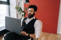 Portrait of Indian business man in formalwear working typing on laptop sitting soft poof in light coworking office on Royalty Free Stock Photo