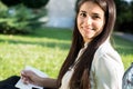 Portrait of an indian girl. Student smiling sitting on green grass writing to notebook Royalty Free Stock Photo