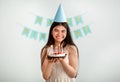 Portrait of Indian teenage girl in festive hat holding birthday cake with candles, smiling at camera indoors Royalty Free Stock Photo