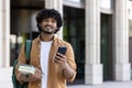 Portrait of Indian young male student with backpack holding phone and books smiling looking at camera while standing on Royalty Free Stock Photo