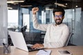 Portrait of an Indian young man working in the office at a laptop, smiling and looking at the camera, raising his hand Royalty Free Stock Photo