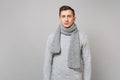 Portrait of indifferent young man in gray sweater, scarf standing isolated on grey wall background in studio. Healthy