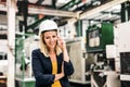 A portrait of an industrial woman engineer on the phone, standing in a factory.