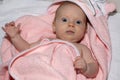 Portrait of Infant baby girl under the pink towel roll looking at camera lying on bed after bath Royalty Free Stock Photo