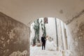 Portrait inside concrete arch of young blonde bride in white dress and brunet groom in suit posing near old city Royalty Free Stock Photo