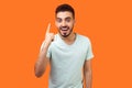 Portrait of inspired handsome brunette man with beard in white t-shirt pointing finger up. indoor studio shot isolated on orange