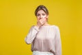 Portrait of intimidated young woman with fair hair in casual beige blouse, isolated on yellow background