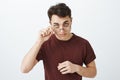 Portrait of intrigued clever european man in red t-shirt, looking from under forehead and taking off glasses, expressing