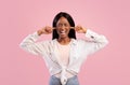 Portrait of irritated young black woman closing ears with fingers and shutting her eyes on pink studio background Royalty Free Stock Photo
