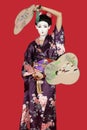 Portrait of Japanese woman in kimono holding fans standing against red background