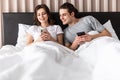 Portrait of a jelous young man looking at his girlfriends mobile phone while sitting together in bed at home