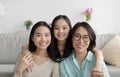 Portrait of joyful Asian family of mature mother, adult daughter and little granddaughter smiling at camera at home Royalty Free Stock Photo
