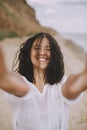 Portrait of joyful boho girl in white shirt having fun on sunny beach. Carefree stylish woman smiling and relaxing on seashore.