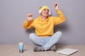 Portrait of joyful cheerful happy man wearing beanie hat, yellow hoodie and jeans posing against gray wall, listening musing with
