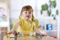 Portrait of joyful child girl toying with statuette of animals in nursery