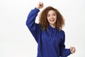 Portrait of joyful curly woman dancing and fist pump, laughing and smiling, rooting for team, winning and celebrating