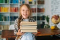 Portrait of joyful elementary child school girl holding stack of books in library at school, looking at camera. Royalty Free Stock Photo