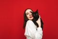 Portrait of a joyful girl hugging with a cute black cat on a red background, looking into the camera and smiling. Happy lady in a Royalty Free Stock Photo