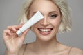 Portrait of a girl with a snow-white smile holding a tube of toothpaste in her hand