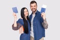 Portrait of joyful glad couple holding passport with flying tickets in hands looking at camera isolated on bright grey background Royalty Free Stock Photo