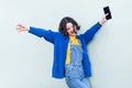 Joyful hipster woman in overalls, listening to music on smart phone, keeps eyes closed, enjoying.