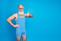 Portrait of joyful pensioner showing thumb up approve sign wearing striped swimwear isolated over blue background Royalty Free Stock Photo