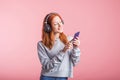 Portrait of a joyful redhead girl who listens to music on headphones with her smartphone in the studio on a pink background. Royalty Free Stock Photo