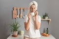 Portrait of joyful satisfied woman in a cosmetic mask and with a towel on her head in the kitchen, smelling pleasant aromat of Royalty Free Stock Photo