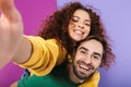 Portrait of joyful smiling couple man and woman in colorful clothing taking selfie photo while doing piggyback ride Royalty Free Stock Photo