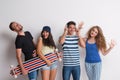 Portrait of joyful young group of friends with longboard standing in a studio.