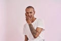 Portrait of joyful young mixed race tattooed man in white t shirt looking at camera, touching his face and smiling while Royalty Free Stock Photo