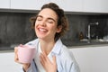 Portrait of a joyful young woman enjoying a cup of coffee at home. Smiling beautiful girl drinks hot tea in morning Royalty Free Stock Photo