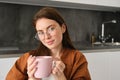 Portrait of a joyful young woman enjoying a cup of coffee at home. Smiling beautiful girl drinks hot tea in winter Royalty Free Stock Photo