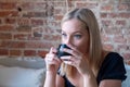 Portrait of joyful young woman enjoying a cup of coffee at home. Smiling pretty girl drinking hot tea in winter. Blonde Royalty Free Stock Photo