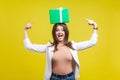 Portrait of joyous brunette woman in jacket and jeans pointing at gift box. indoor studio shot, yellow background