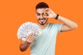 Portrait Of Joyous Rich Brunette Man Holding Dollars And Covering One Eye With Golden Bitcoin. Isolated On Orange Background
