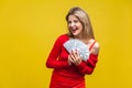 Portrait of joyous wealthy beautiful woman in red dress holding money, isolated on yellow background