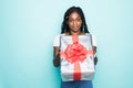 Portrait of joyous african woman with afro hairdo holding gift box and smiling in happiness over blue background