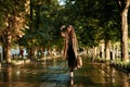 Portrait of joyous woman using cell phone while walking through empty alley