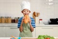 Portrait of kid eating large loaves of bread, happy Asian boy with apron and chef hat holding and eating freshly baked homemade Royalty Free Stock Photo